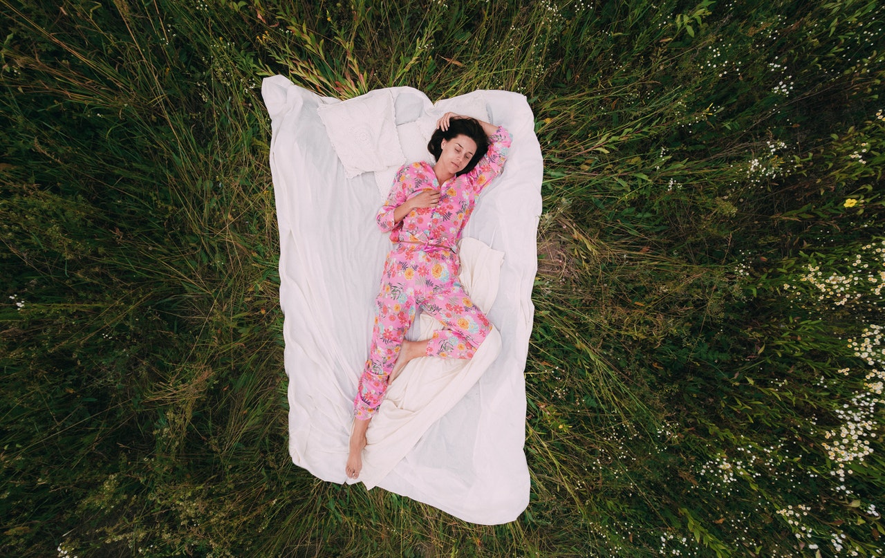 Woman in Pink Floral Pajama Lying On a White Sheet Surrounded With Grass