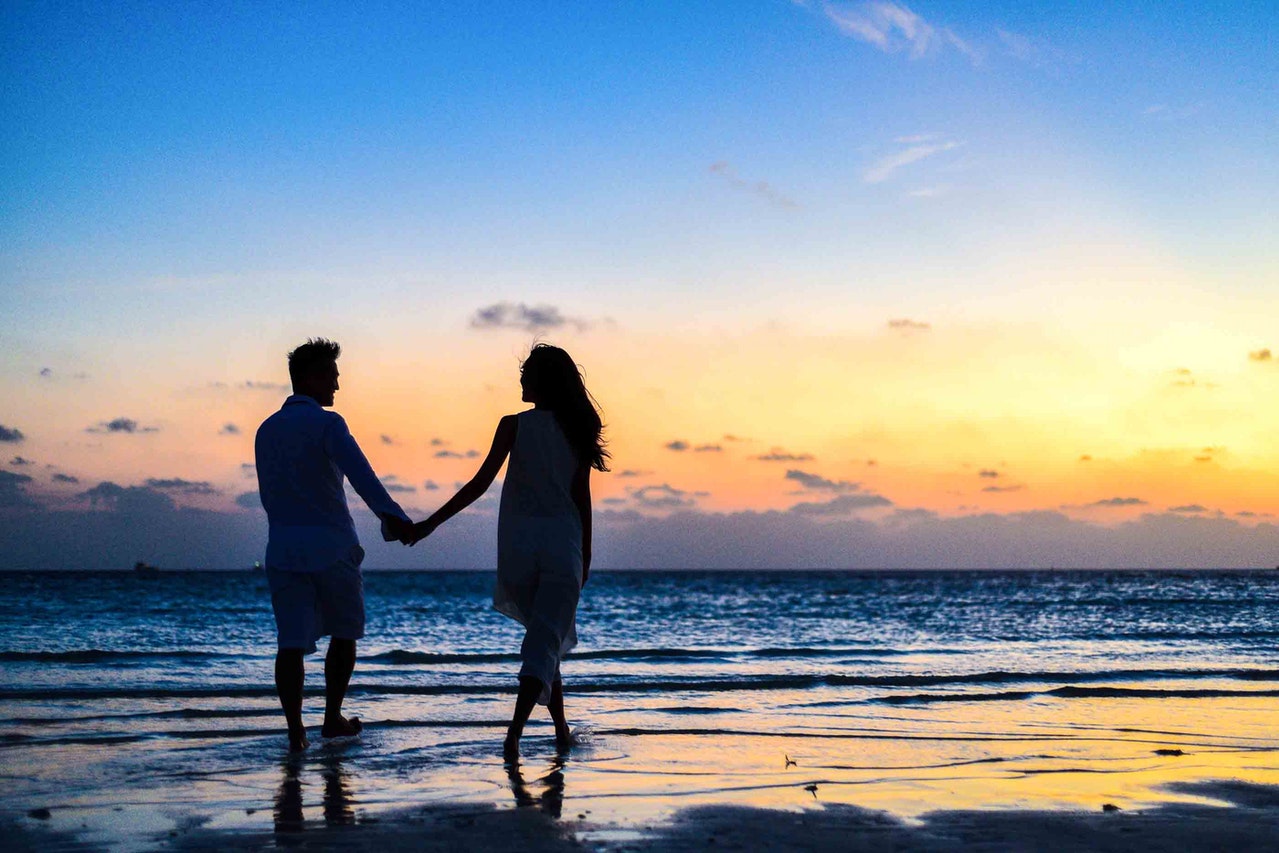 A Man and a Woman Holding Hands While Walking on the Seashore during Sunrise