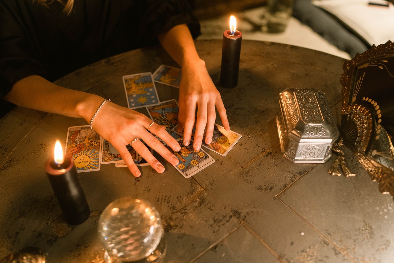 Hands Touching the Tarot Cards on the Table With Two Candles