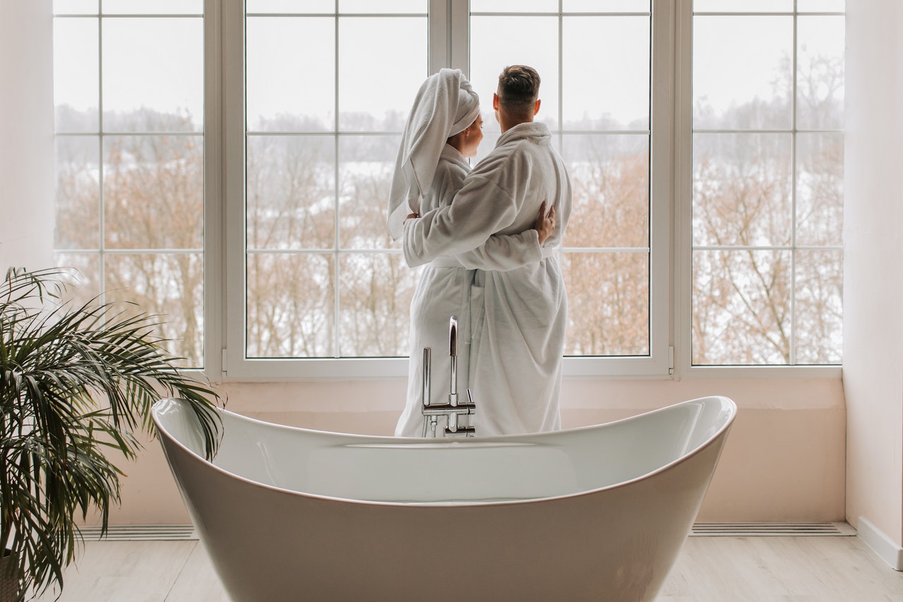 Man and Woman Wearing Bathrobes Standing And Looking Out The Window