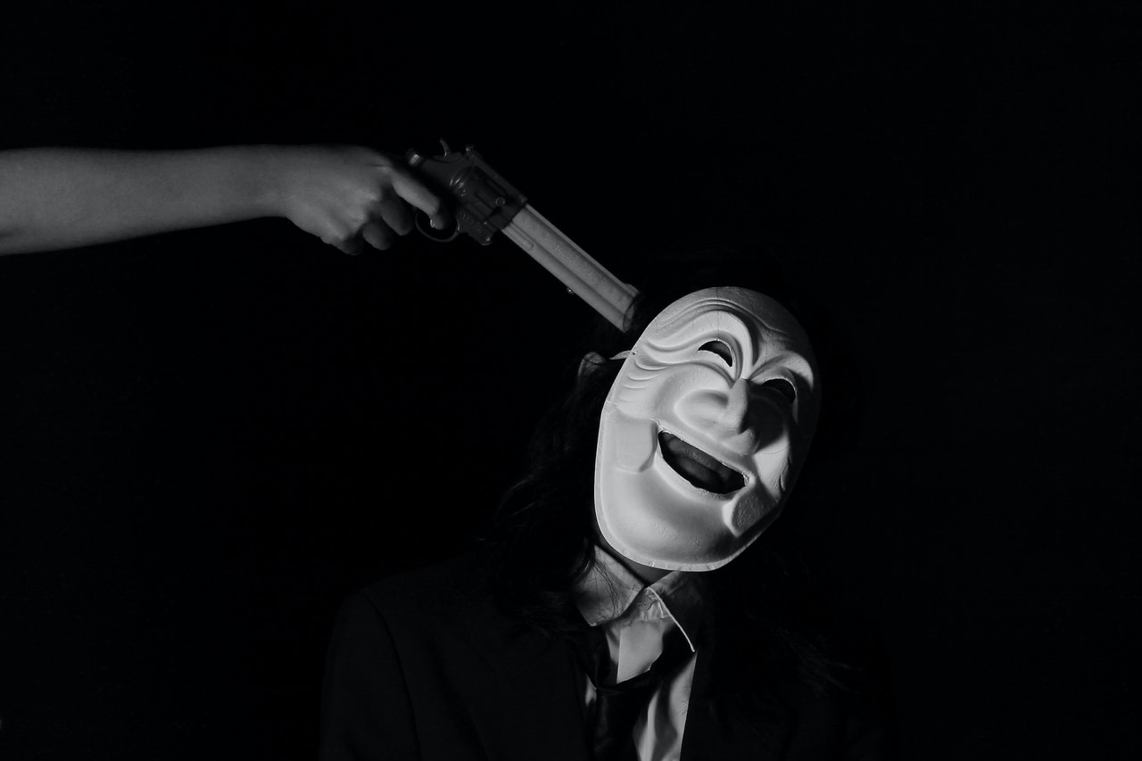 Person pointing a gun to man with a mask