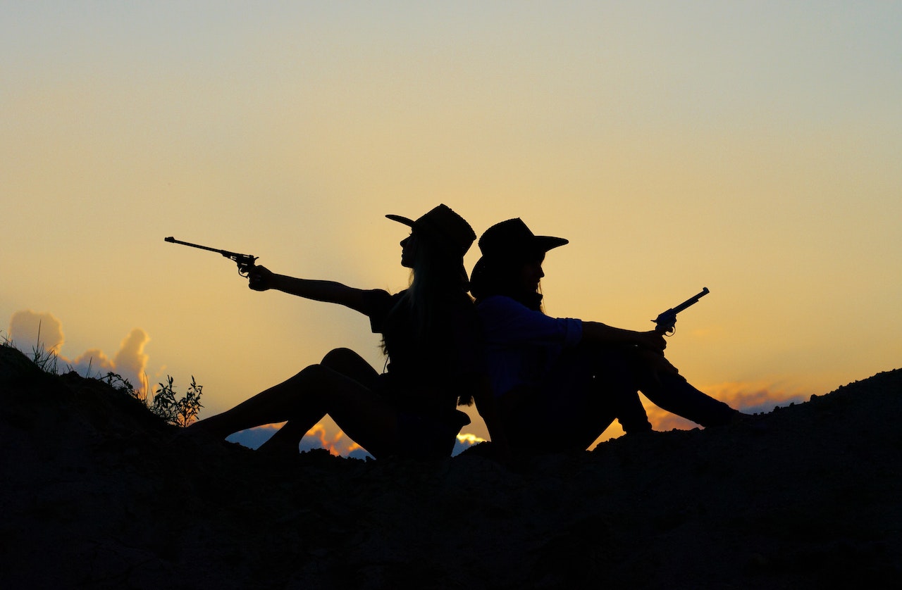 Silhouette of Two People Holding Revolver Pistols Sitting on Hill