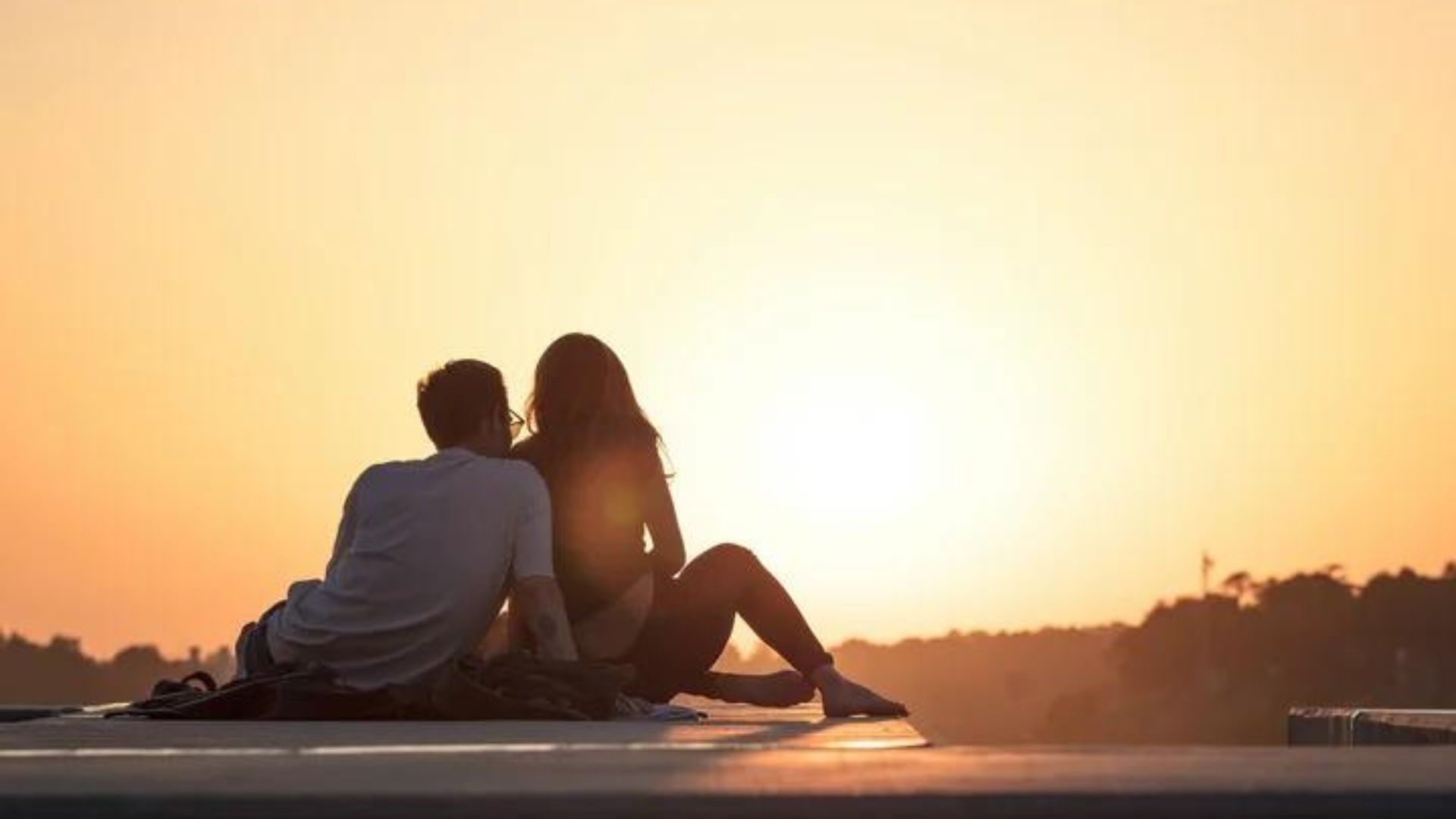 Couple Sitting On A Boardwalk And Enjoying The Sunset