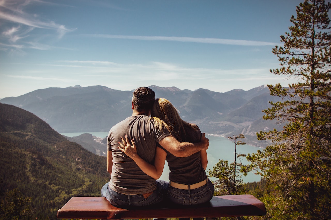 Man and Woman Sitting on Bench Overlooking The Lake And Mountains