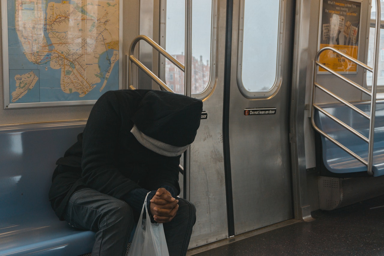 Person in Black Hoodie Sitting on Train Bench with head down