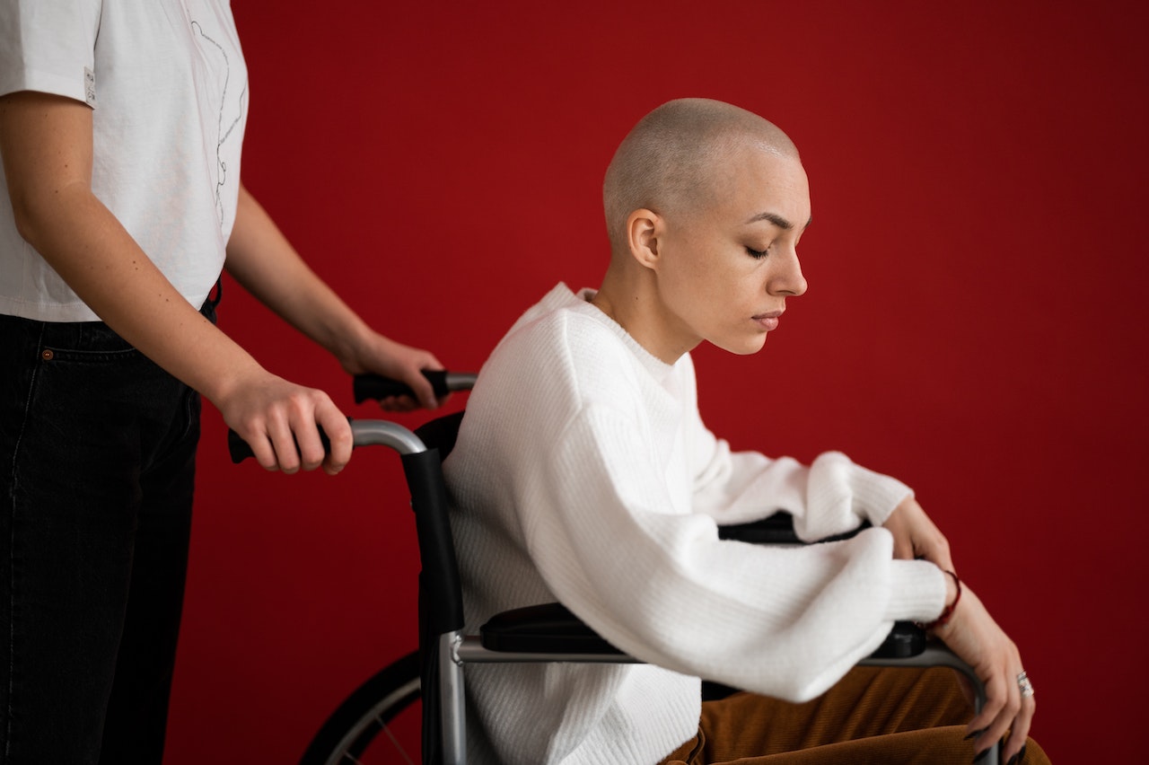 Crop assistant pushing wheelchair with sick patient on red background