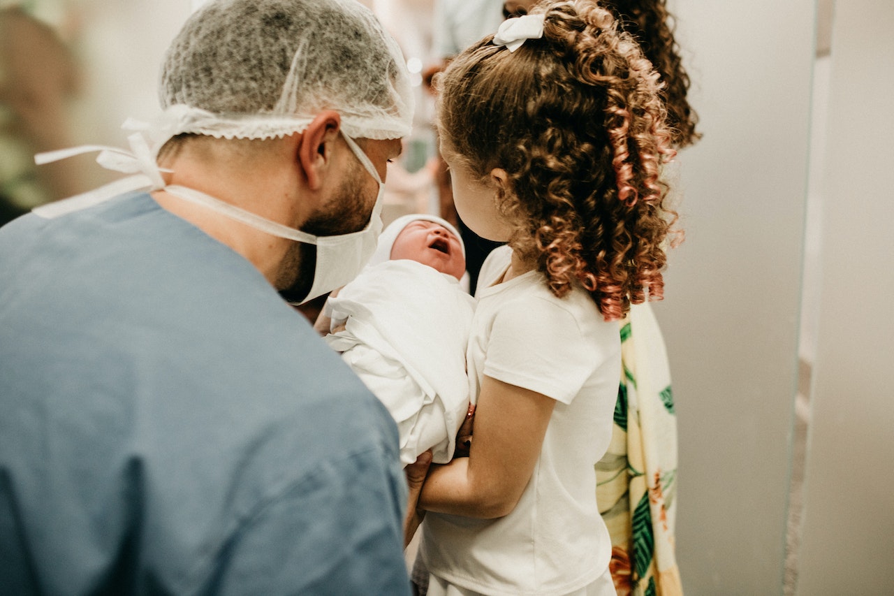 Man in scrubs handing baby to curly haired girl