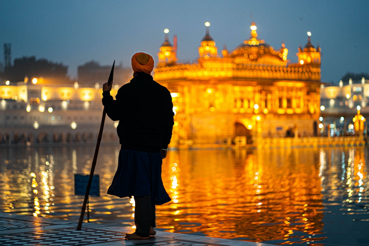 Man with turban holding a stick looking at a golden temple