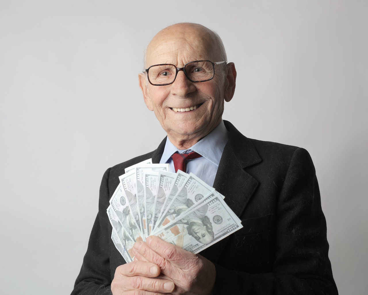 Old Man With Eyeglasses In Black Suit Holding Dollar Bills