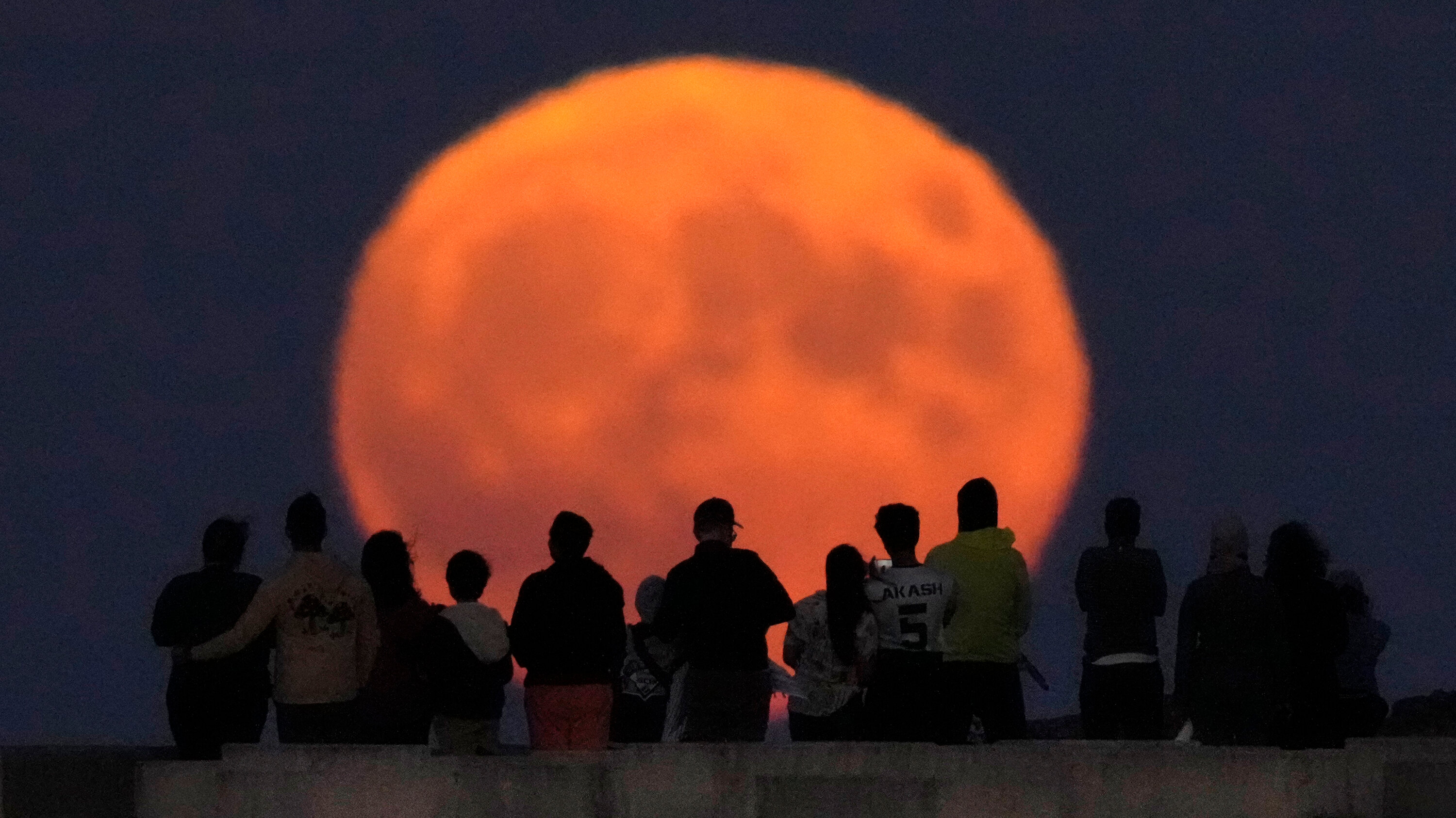 A Group Of People Looking at an Orange Moon