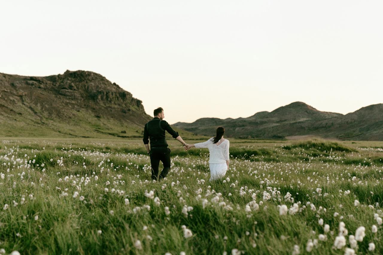 A Couple Walking Hand in Hand on Grass Field with Wildflowers